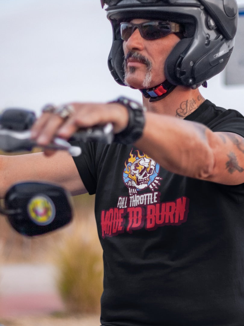 Biker wearing a black 'Full Throttle - Made to Burn' graphic t-shirt, riding a custom motorcycle with rugged desert scenery in the background.