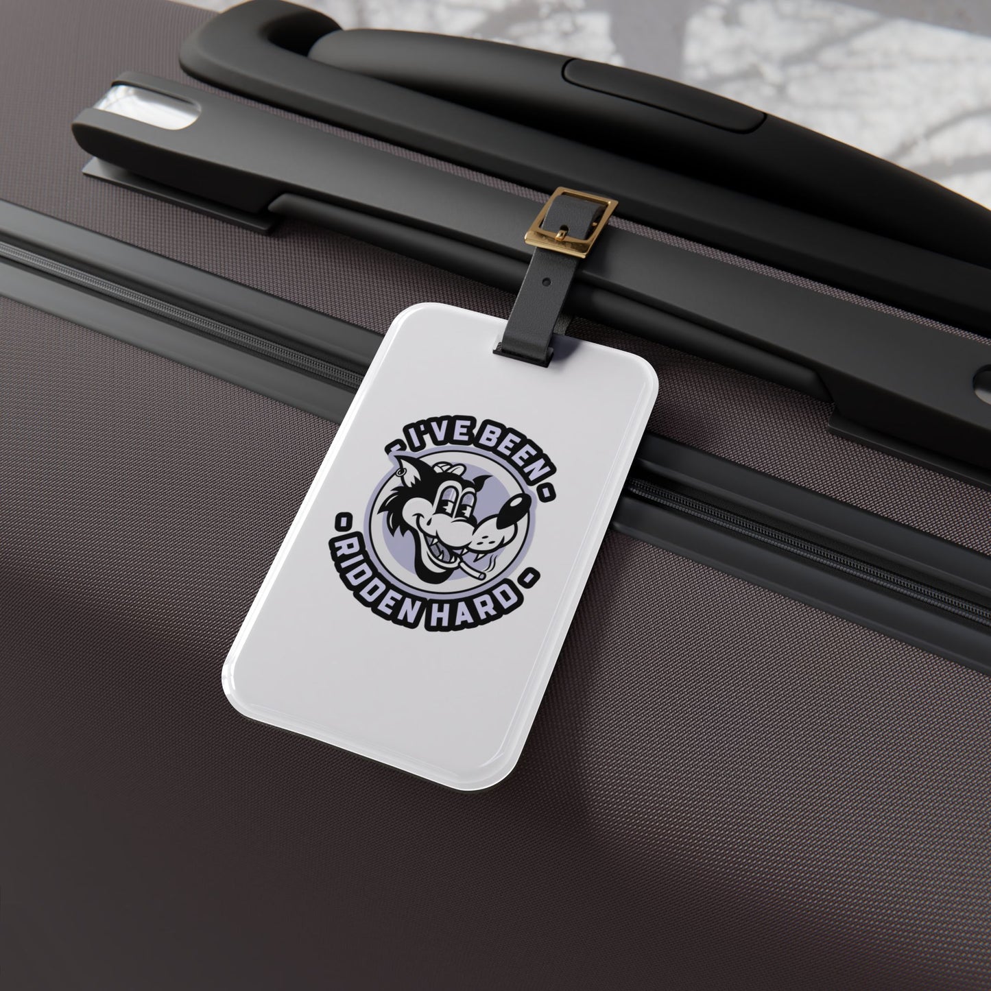 Luggage tag featuring a vintage-style wolf graphic with the phrase "I've Been Ridden Hard", attached to a suitcase.