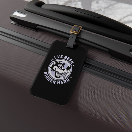 Luggage tag featuring a vintage-style wolf graphic with the phrase "I've Been Ridden Hard", attached to a suitcase.