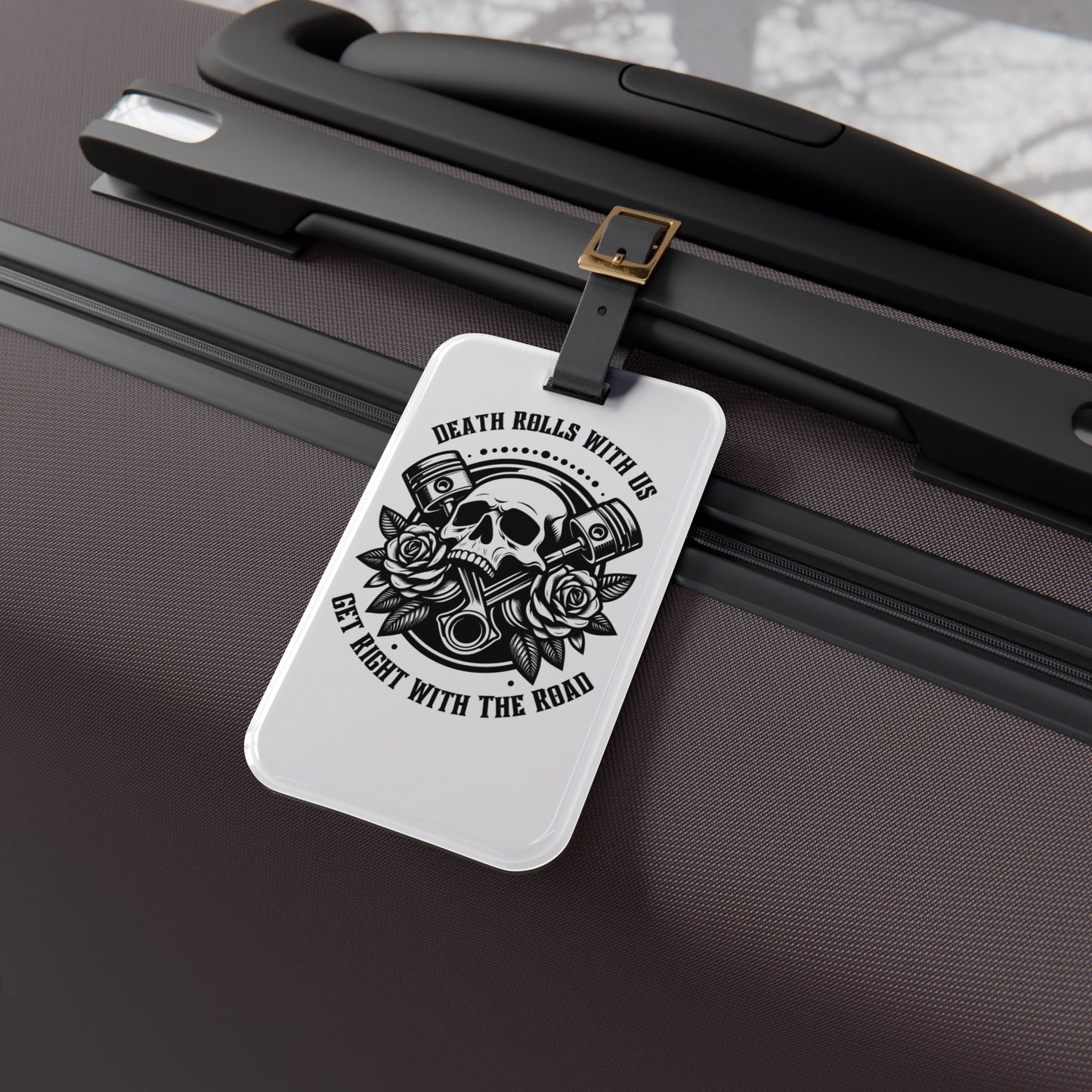 Luggage tag featuring a skull, pistons, and roses with the phrase "Death Rolls With Us – Get Right With the Road", attached to a suitcase.