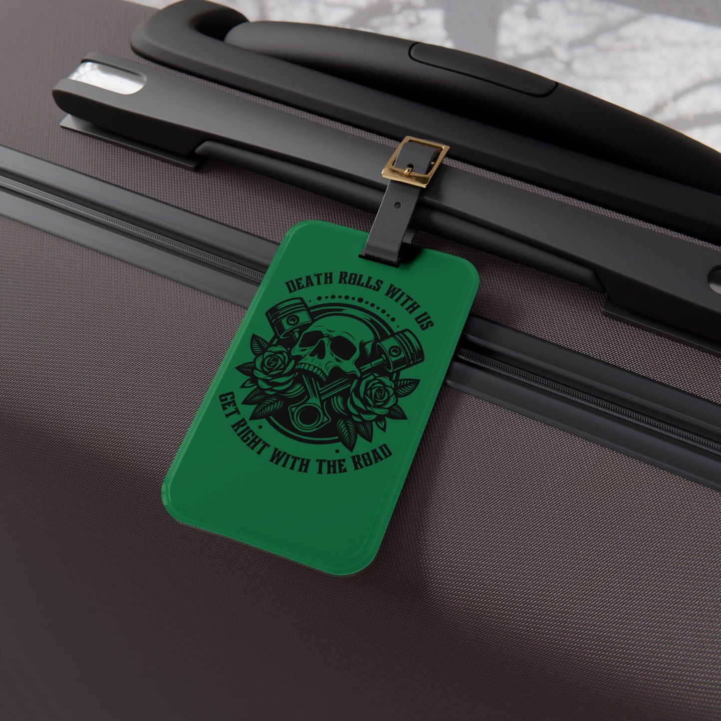 Luggage tag featuring a skull, pistons, and roses with the phrase "Death Rolls With Us – Get Right With the Road", attached to a suitcase.