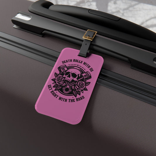 Luggage tag featuring a skull, pistons, and roses with the phrase "Death Rolls With Us – Get Right With the Road", attached to a suitcase.