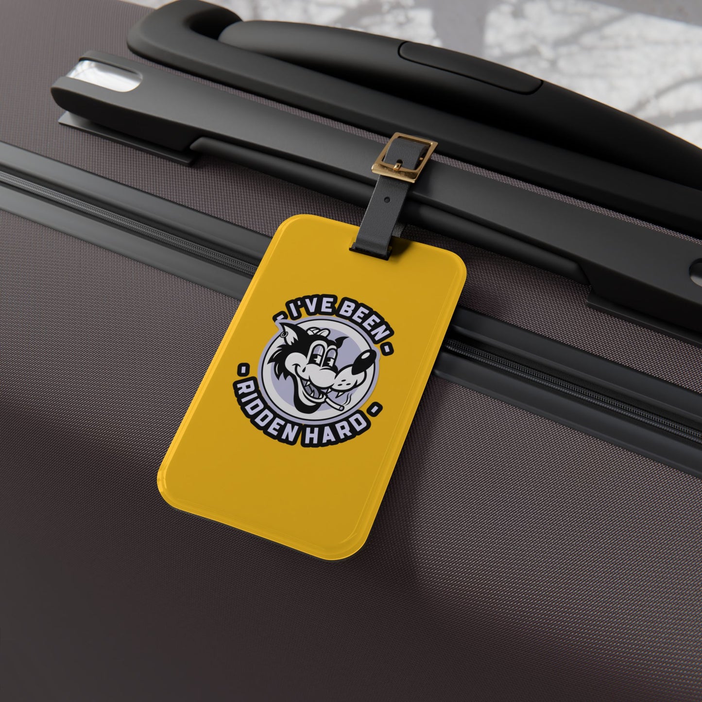 Luggage tag featuring a vintage-style wolf graphic with the phrase "I've Been Ridden Hard", attached to a suitcase.